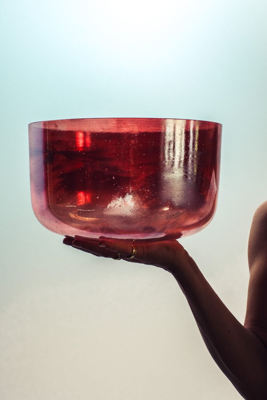 Een hand houdt een grote roze kristallen klankschaal omhoog tegen een zachte lucht
